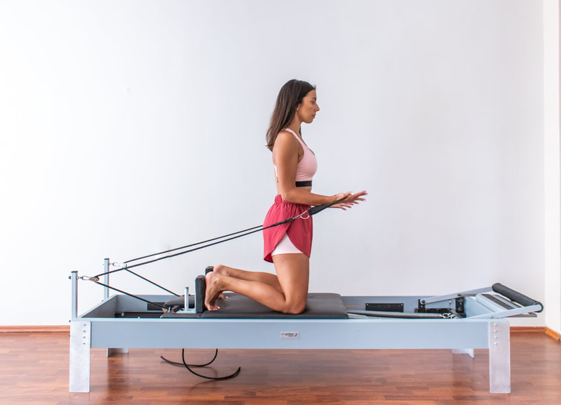 Woman kneeling on a Pilates Reformer doing arm exercises