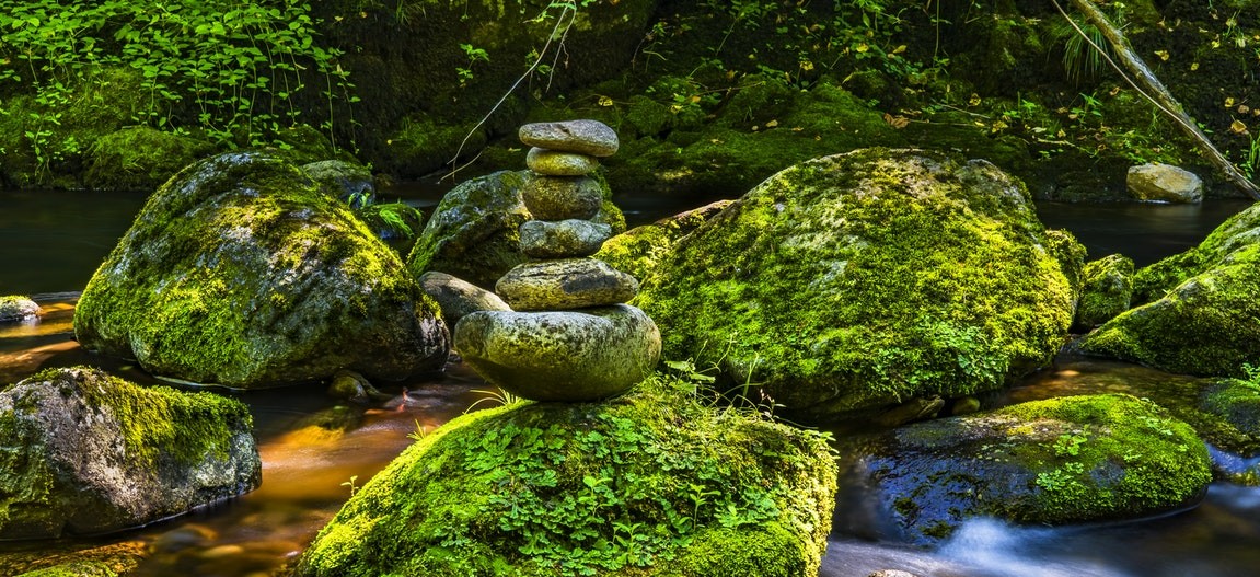 Beautiful stream with moss covered boulders and a cairn balanced on one in the center.